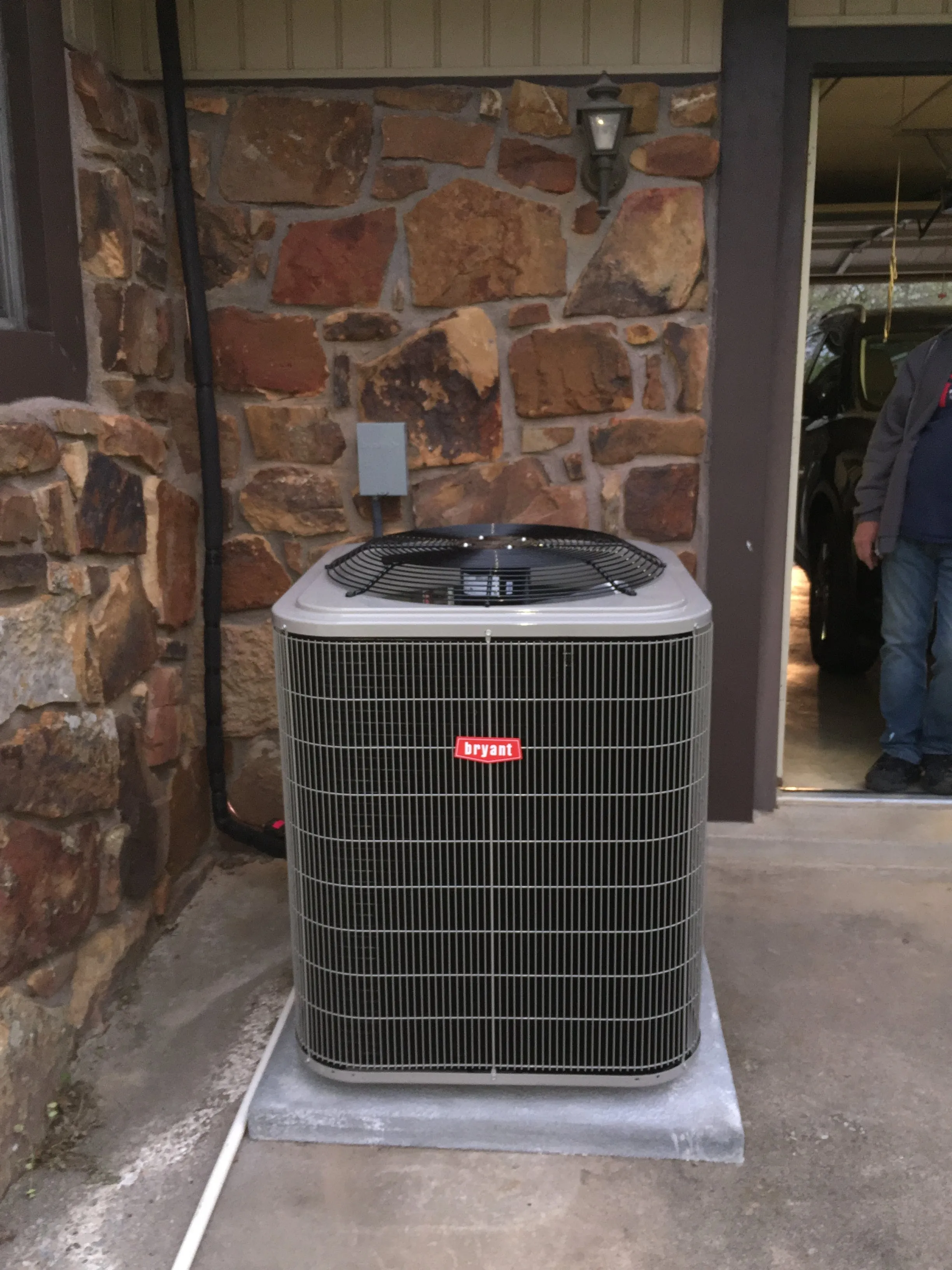 A new Bryant AC condenser on a concrete pad beside a stone house
