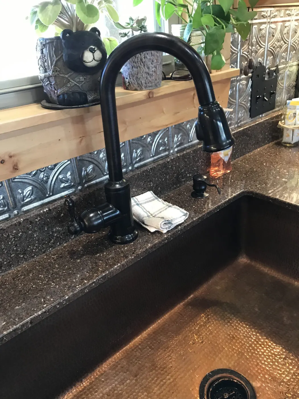 A black pull-down kitchen faucet over a hammered copper farmhouse sink