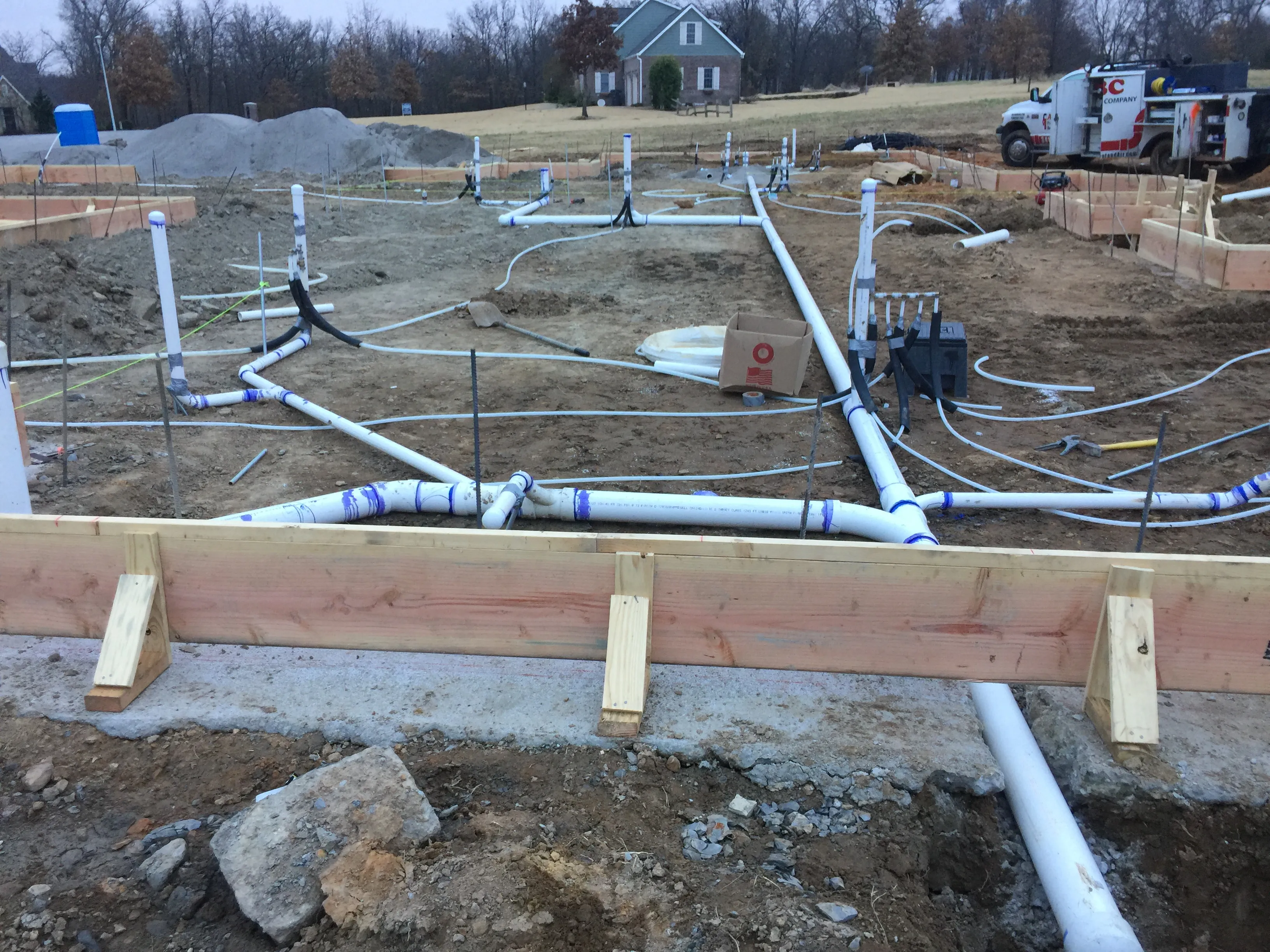 A large foundation plumbing rough-in at dusk with ABC's truck in the background and PVC drain lines across the slab