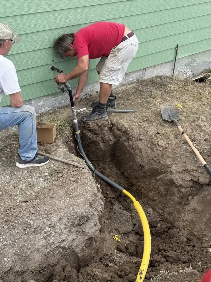 Two crew members connecting a new gas line in a trench beside a house