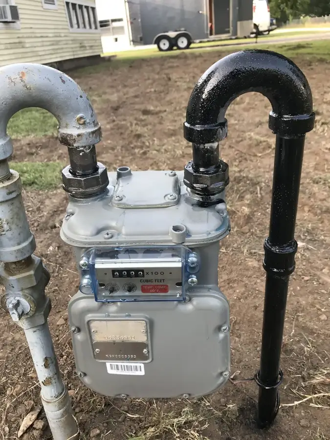 A residential gas meter with new black iron piping beside a house