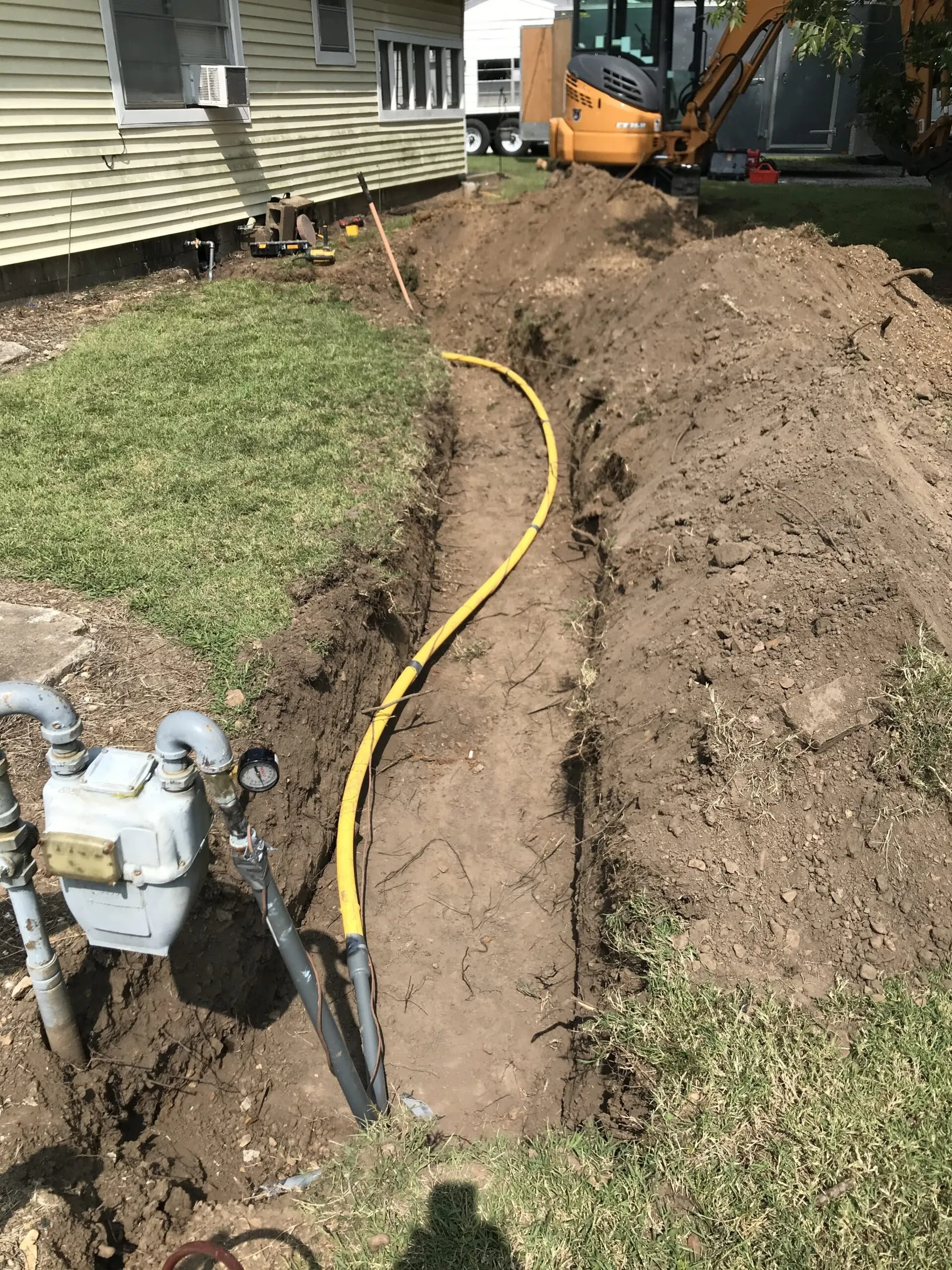 A long trench with a yellow gas line and an excavator working in the background