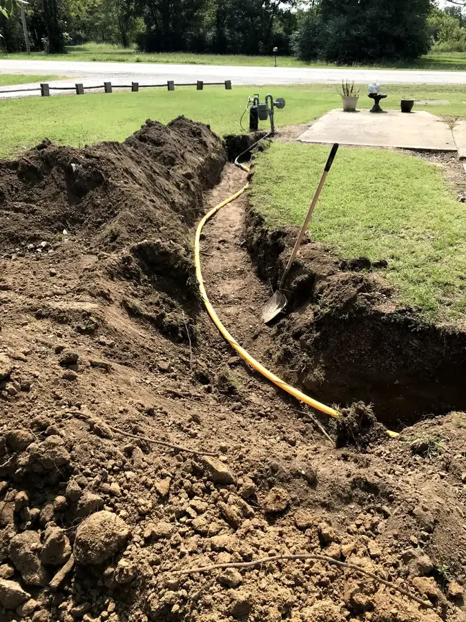A yellow poly gas line laid in a fresh trench running across a lawn toward a house