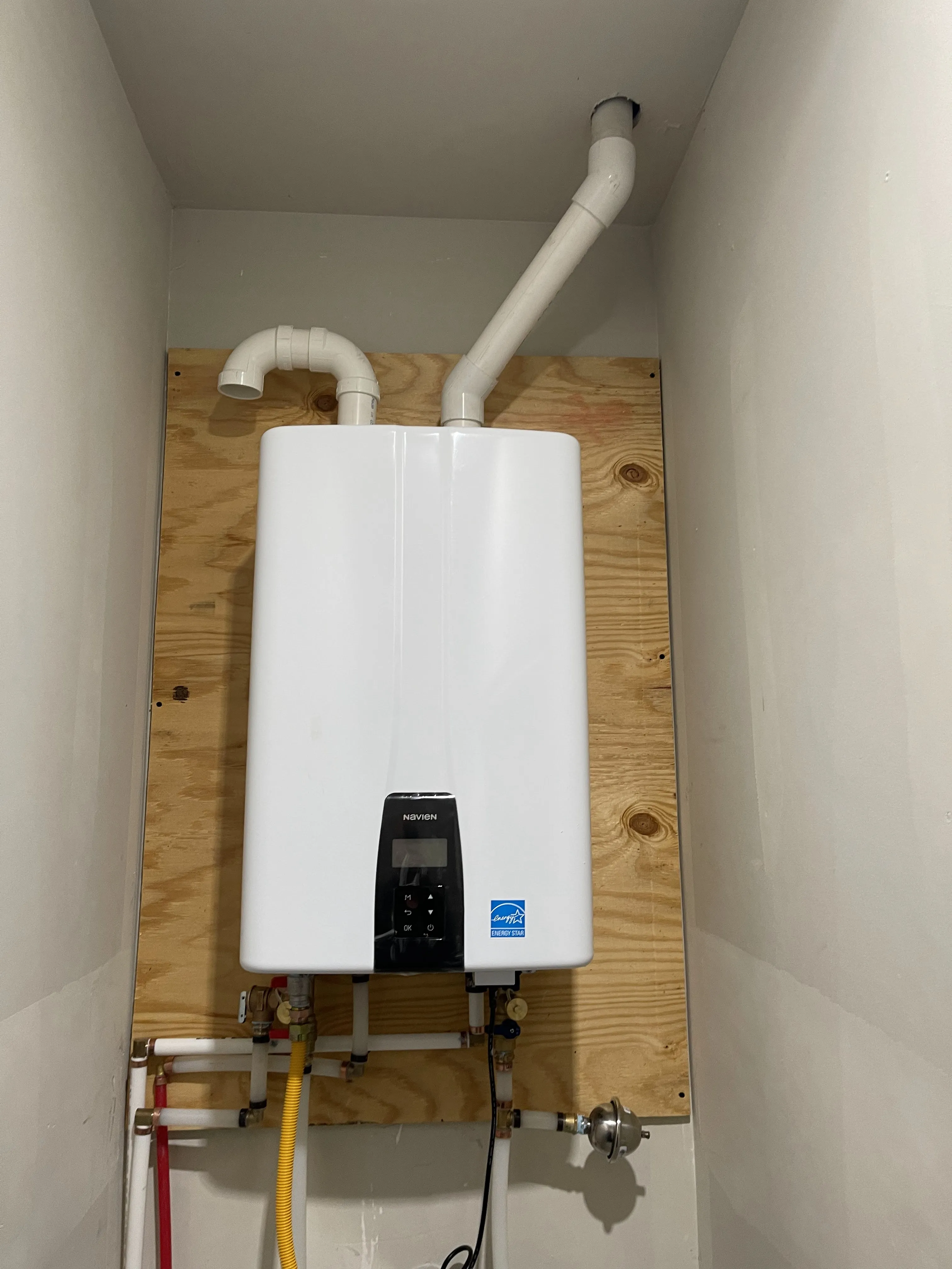 A new Navien tankless water heater mounted on a plywood backer board with PVC venting