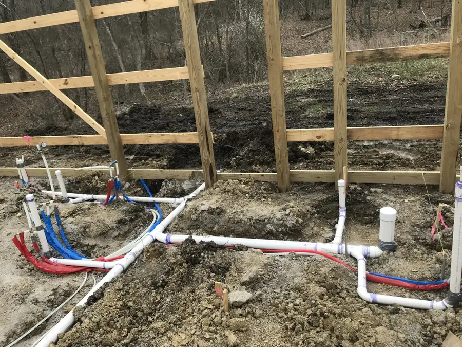 Plumbing rough-in for a new building: white PVC drains with red and blue PEX lines laid out in the dirt before the slab is poured