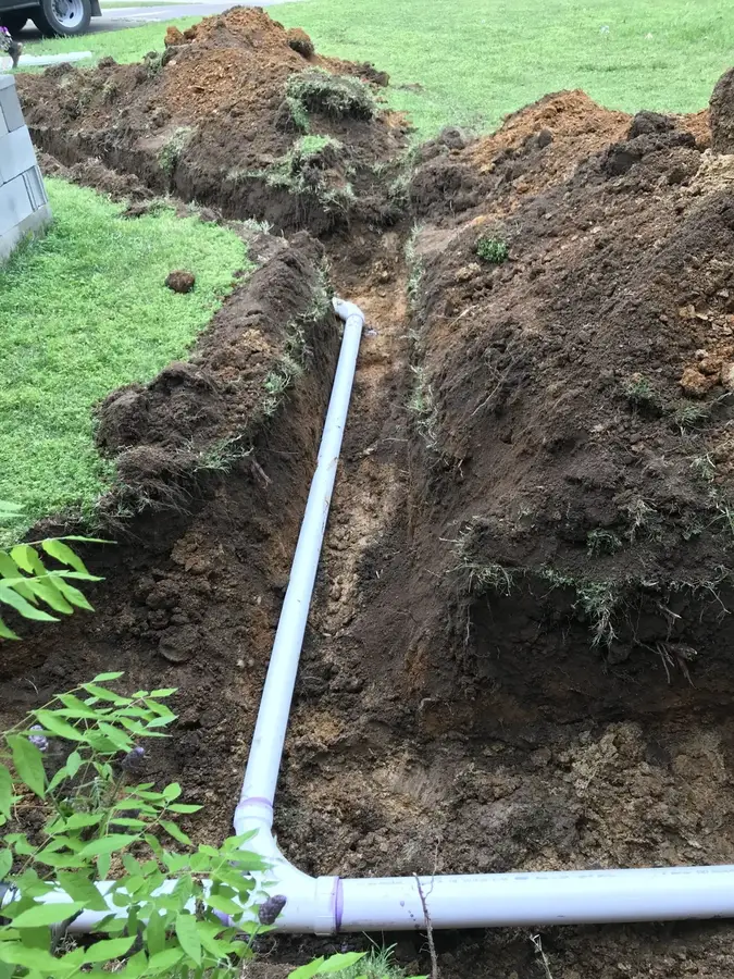 A new white PVC sewer line with a wye fitting laid in a trench beside a house