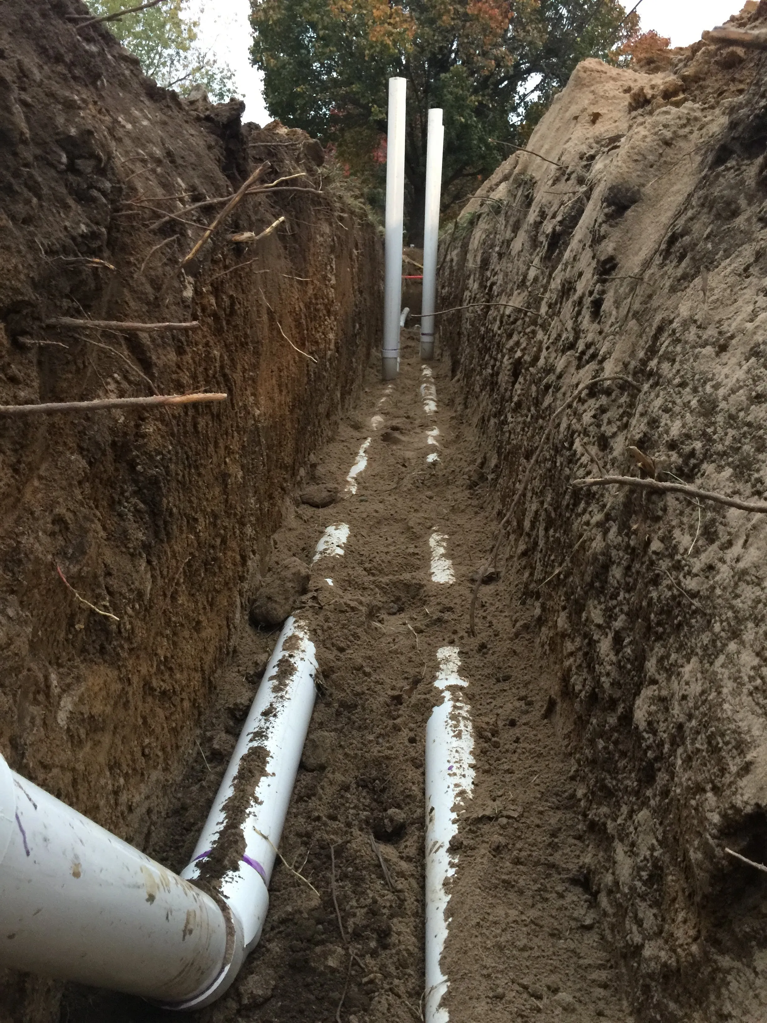 A deep trench with new PVC sewer pipe and risers laid in gravel bedding