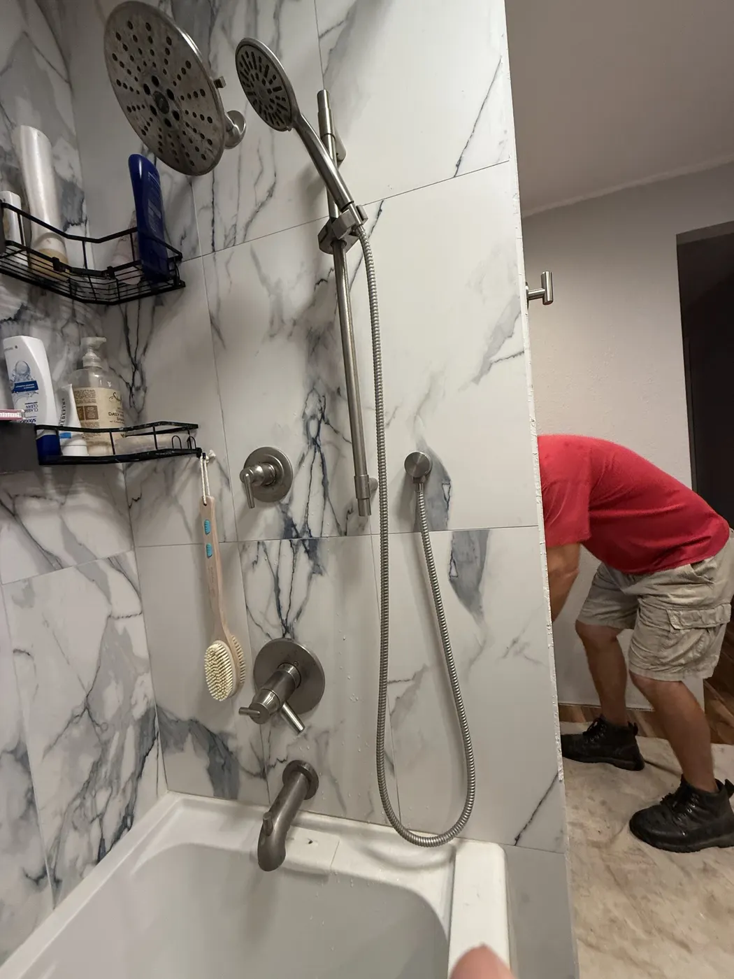 A finished tub and shower with marble-look wall panels and a handheld shower head