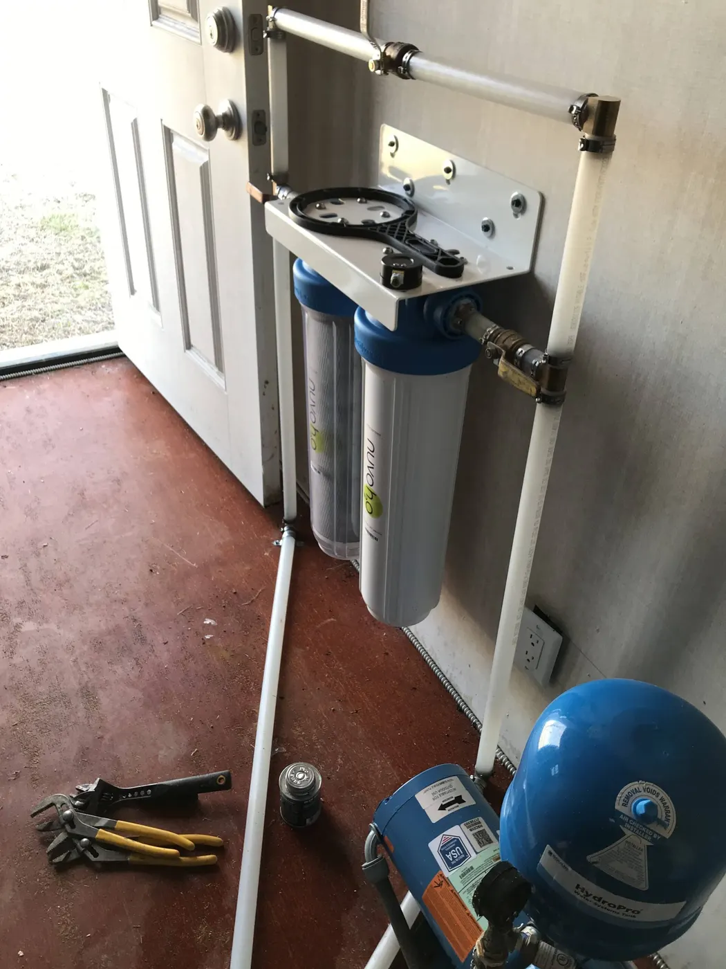 Two blue whole-house water filters plumbed next to a well pressure tank